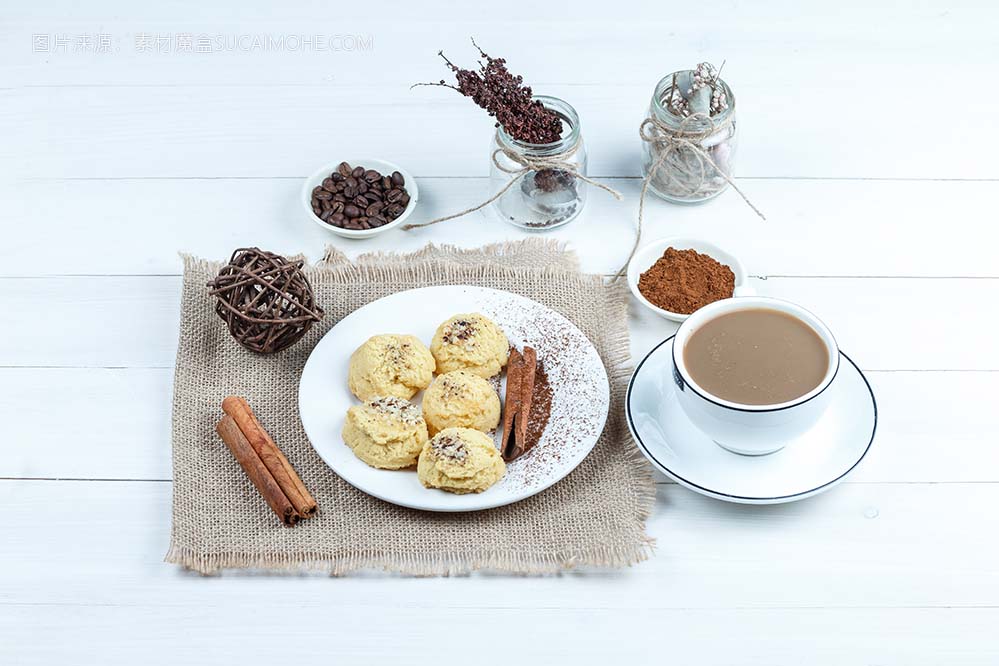 高角度视图饼干、肉桂、绳索在麻袋上，上面放着一碗速溶咖啡，白色木板背景上有一杯咖啡