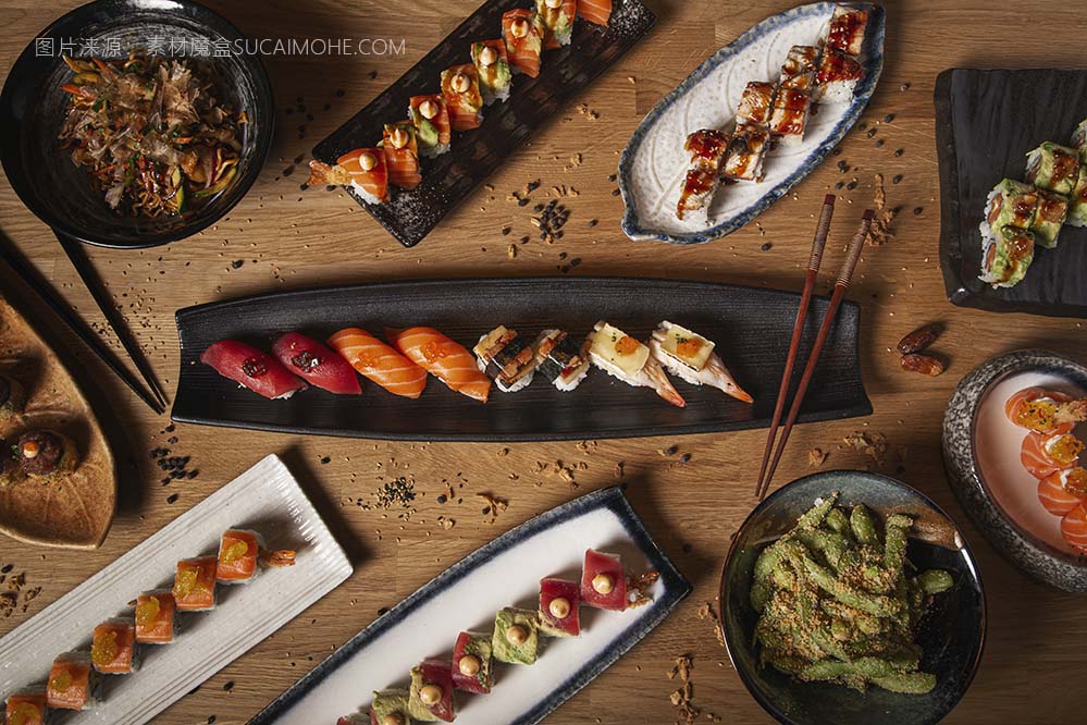 餐厅木桌上的各种寿司、握寿司、生鱼片、日式炒面和毛豆的顶视图