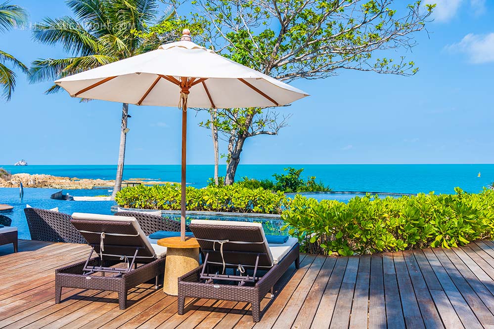 遮阳伞和椅子在酒店室外游泳池周围的度假胜地，海景度假旅行免