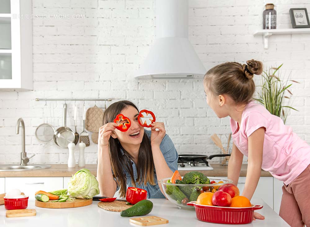 妈妈和女儿在厨房里准备一份沙拉。玩得开心，玩蔬菜。健康的饮食习惯和生活方式的概念。