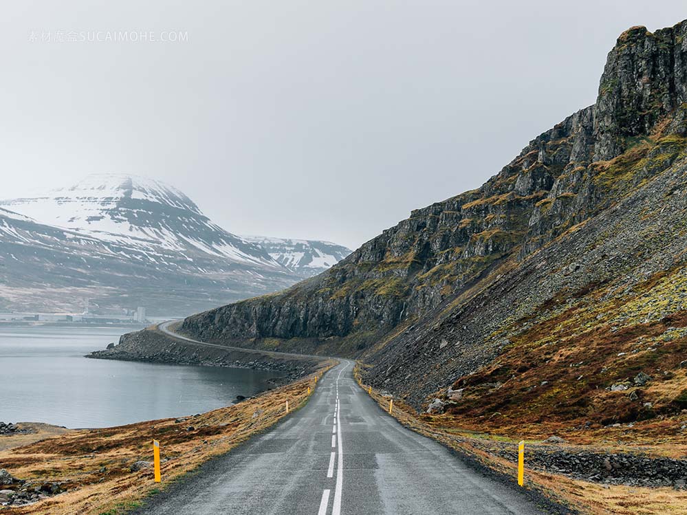 弯曲的道路被大海和岩石包围，在绿色的天空和雪覆盖在多云的天空下curvy-road-surrounded-by-sea