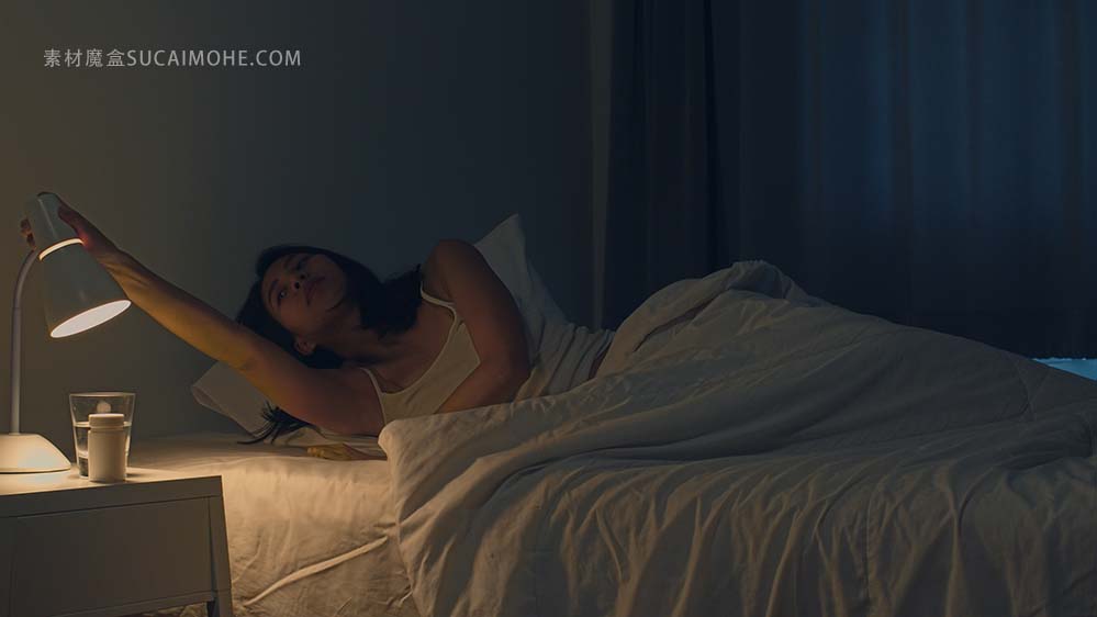 舒适地睡觉在她的卧室的美丽的亚裔少妇。印度女性的手关闭电灯开关，在房间里的床在家里
