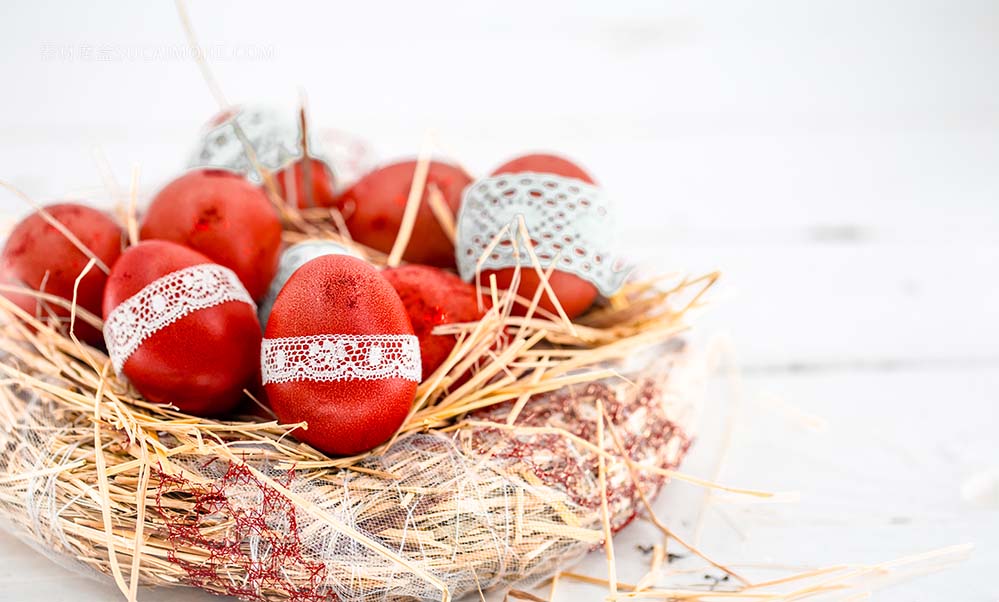 在干草巢中的红色复活节彩蛋，绑上花边丝带，特写，躺在白色的木头上d的照片red-easter-eggs