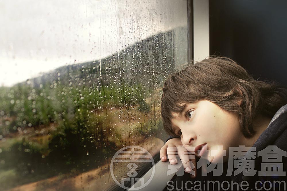 小男孩坐在被雨水打湿的火车玻璃窗旁出神