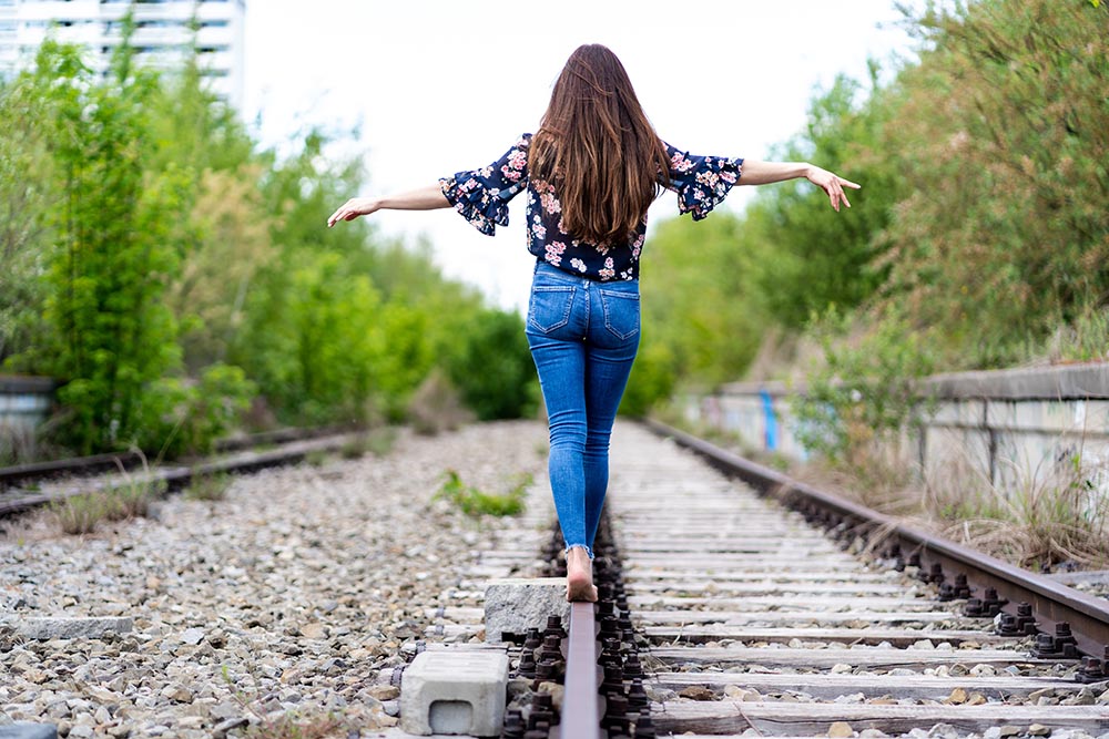 一位年轻女性赤脚穿过火车轨道并试图保持平衡的背部
