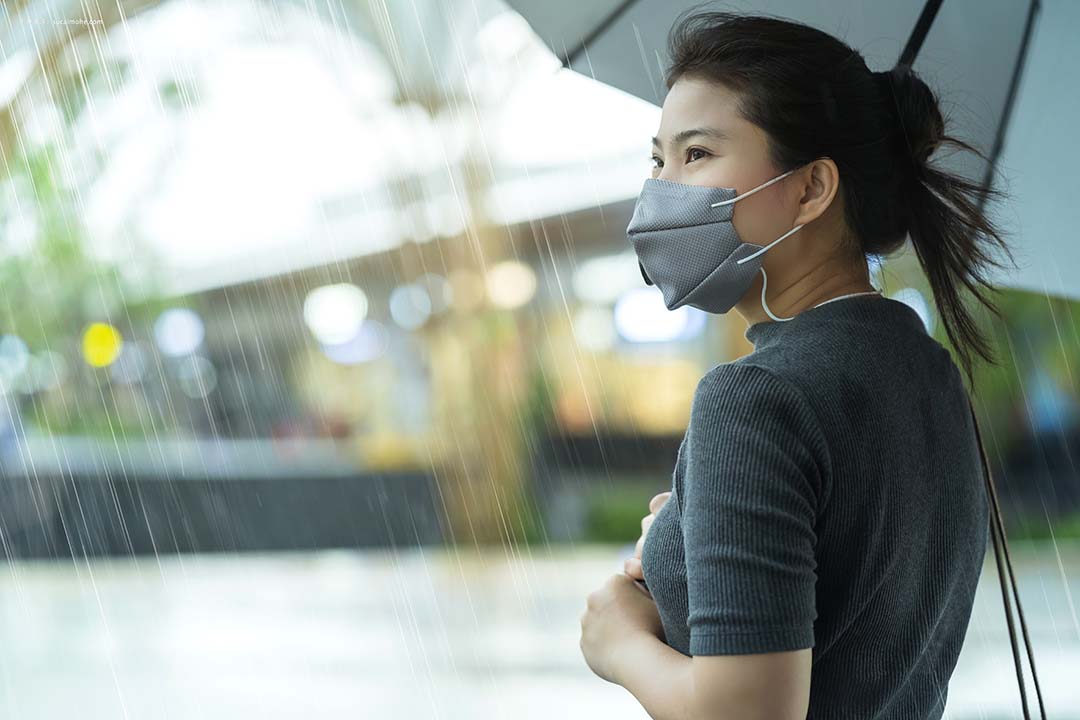 亚洲女性戴口罩独自站着手持遮影雨季大雨户外街道边