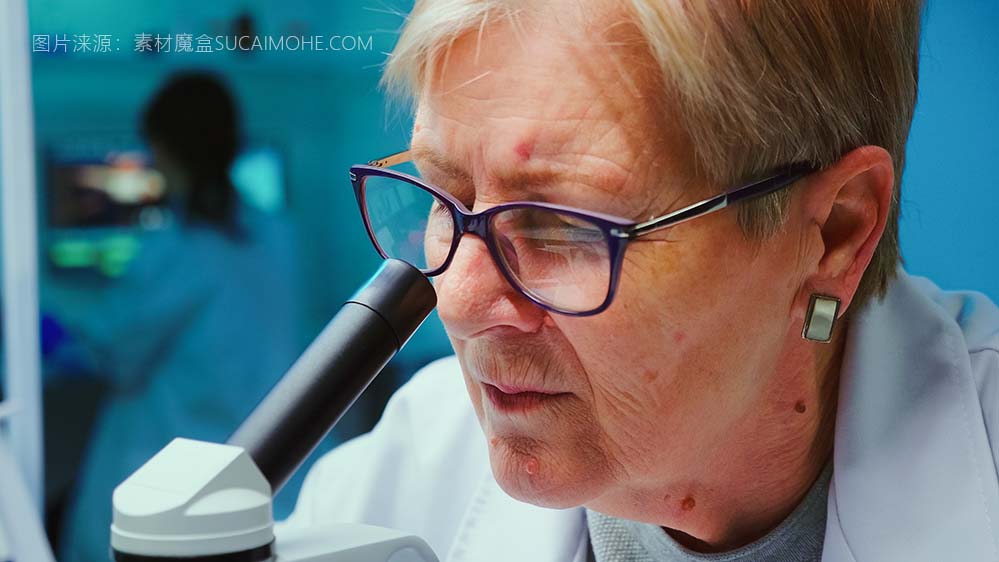 使用显微镜进行研究的资深科学家的特写，而同事们则在现代设备齐全的实验室从事背景工作